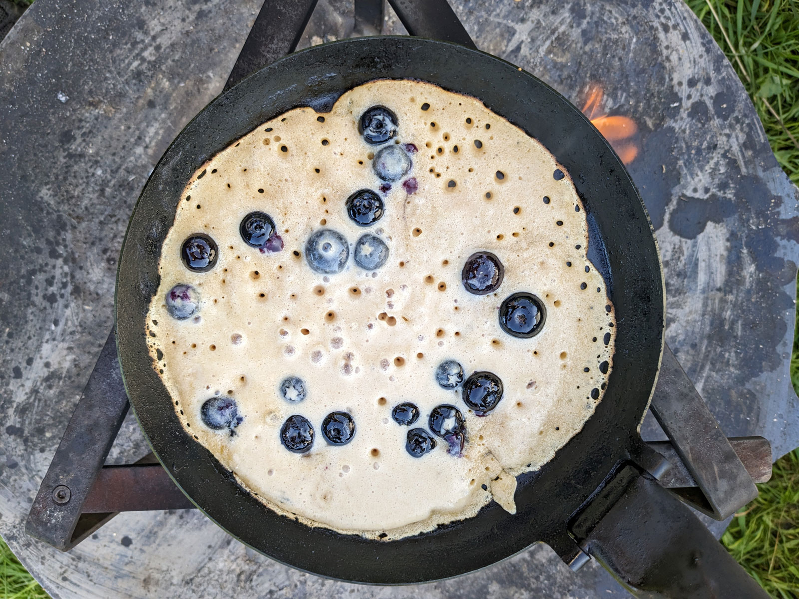 Pfannkuchen mit Blaubeeren über dem Lagerfeuer in der Eisenpfanne.